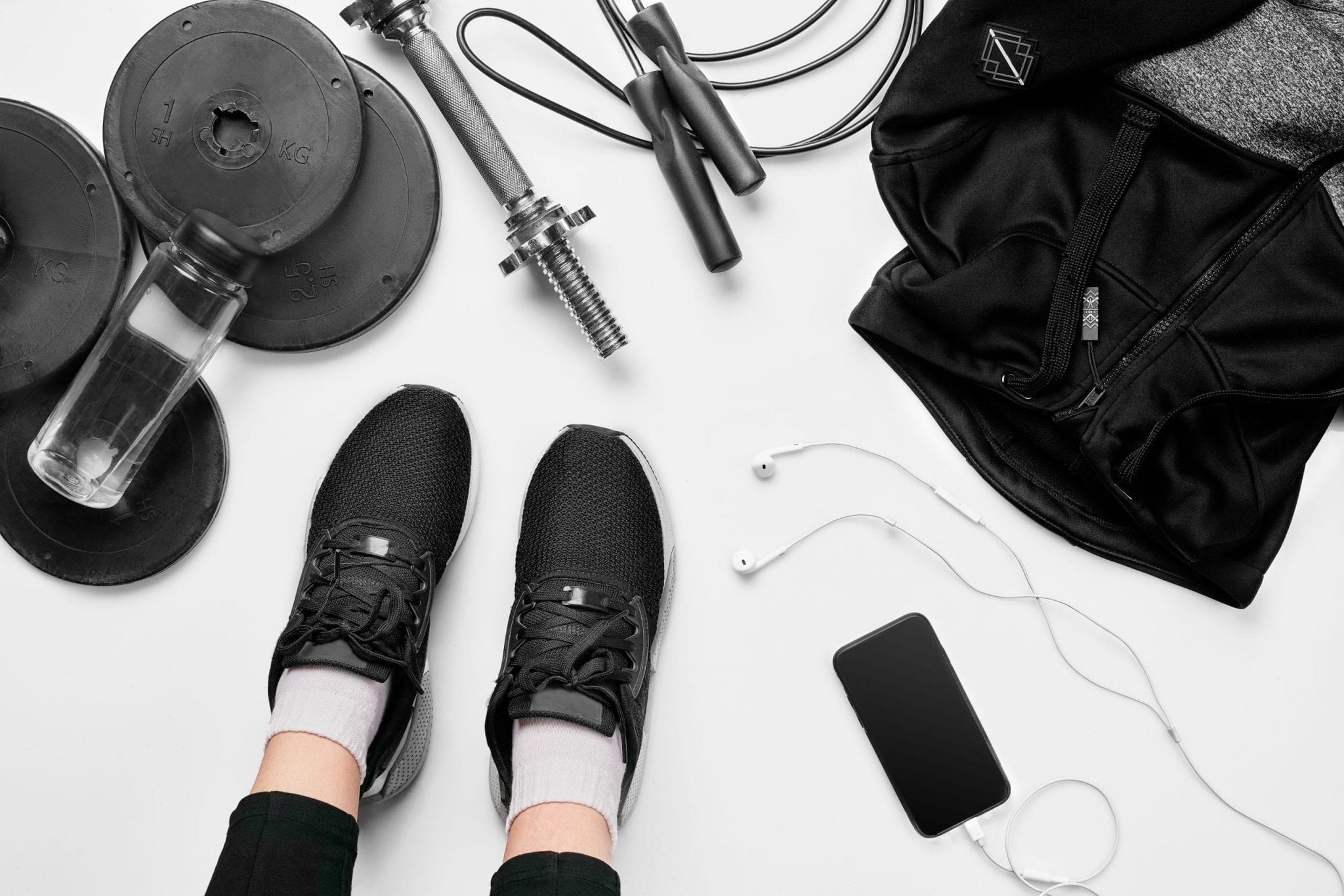 Women’s legs in sneakers, fitness clothing, smartphone, dumbbells, headphones, top view.